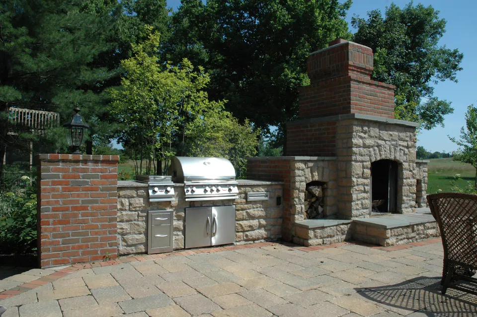 Stone grill counter with two built-in grills beside a large stone and brick outdoor fireplace
